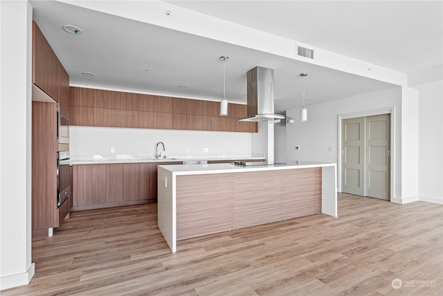 kitchen with oven, hanging light fixtures, island range hood, and light hardwood / wood-style floors