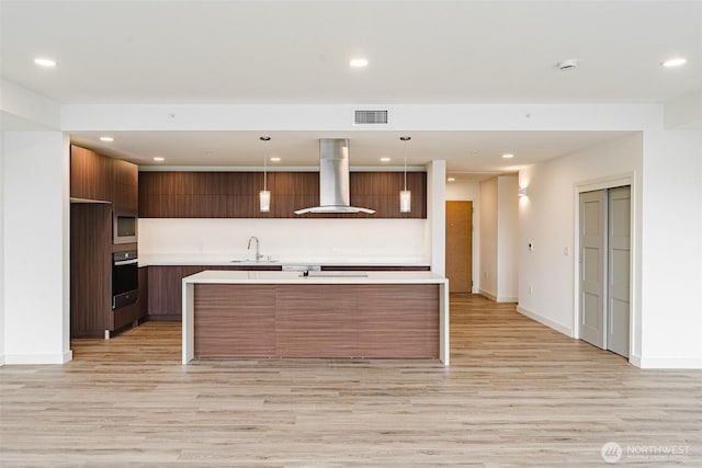 kitchen with oven, a sink, visible vents, modern cabinets, and island exhaust hood