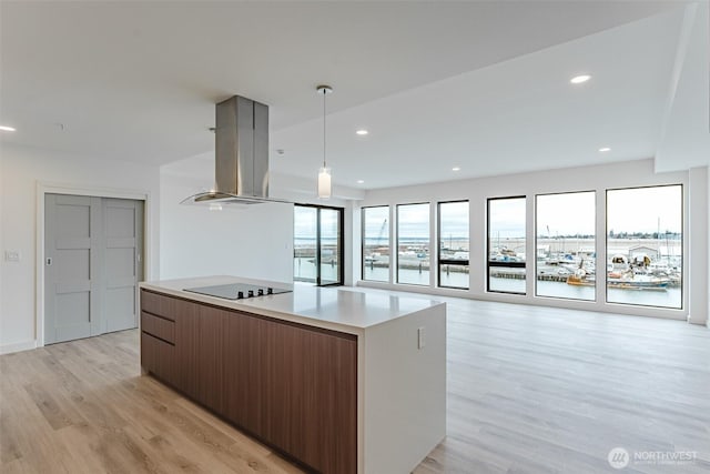 kitchen featuring black electric stovetop, island range hood, a kitchen island, light wood-type flooring, and modern cabinets