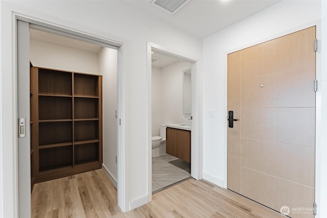 hall featuring light wood-style flooring, a sink, visible vents, and baseboards