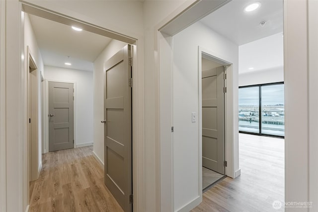 corridor featuring baseboards, light wood finished floors, and recessed lighting