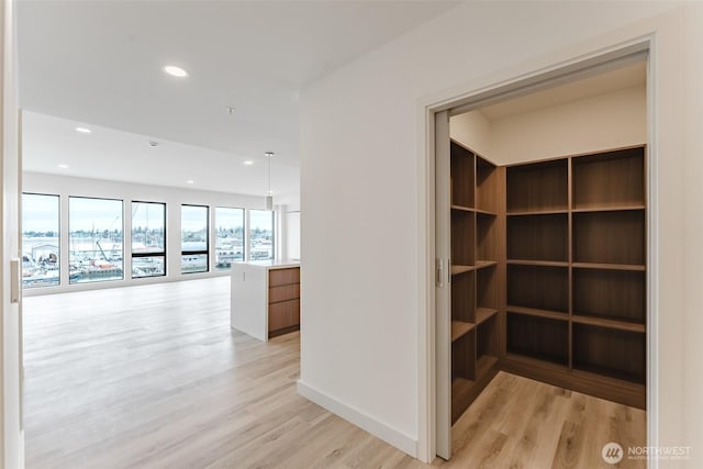 hall featuring baseboards, light wood-type flooring, and recessed lighting