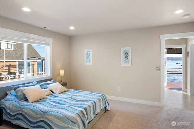 bedroom featuring light carpet, a water view, and multiple windows