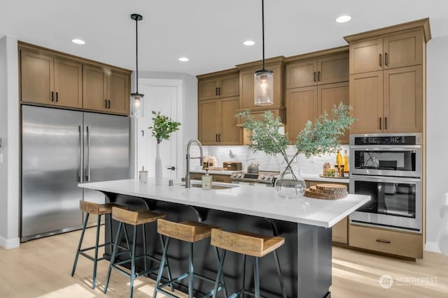 kitchen with appliances with stainless steel finishes, sink, a kitchen breakfast bar, hanging light fixtures, and a kitchen island with sink