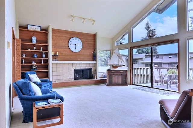 carpeted living room featuring a tile fireplace, rail lighting, and a high ceiling