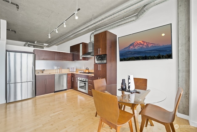 kitchen with sink, appliances with stainless steel finishes, track lighting, wall chimney exhaust hood, and light wood-type flooring