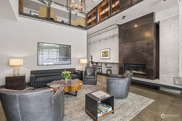 living room featuring finished concrete floors, a glass covered fireplace, track lighting, and a high ceiling