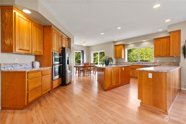 kitchen featuring light stone counters, appliances with stainless steel finishes, a center island, and light wood-type flooring