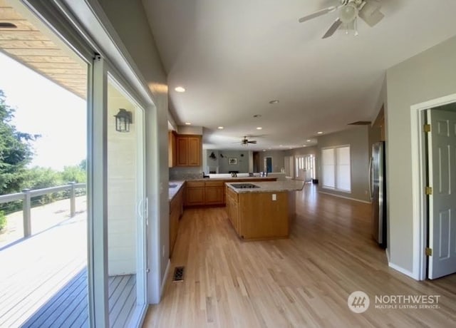 kitchen featuring a center island, light wood-type flooring, stainless steel refrigerator, kitchen peninsula, and ceiling fan