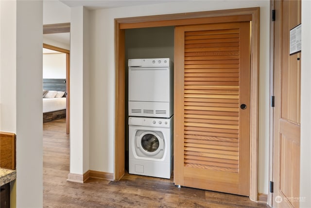 clothes washing area with stacked washer and dryer and hardwood / wood-style flooring