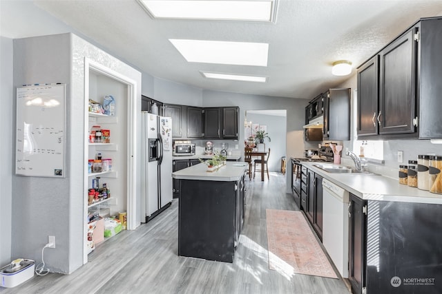 kitchen featuring a skylight, sink, white appliances, and light wood-type flooring