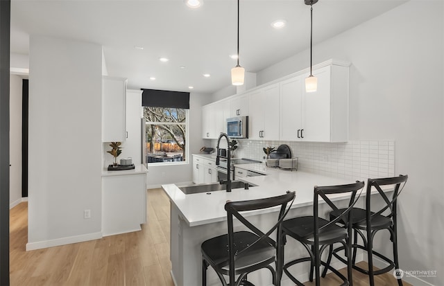 kitchen with decorative light fixtures, light hardwood / wood-style flooring, kitchen peninsula, stainless steel microwave, and a breakfast bar