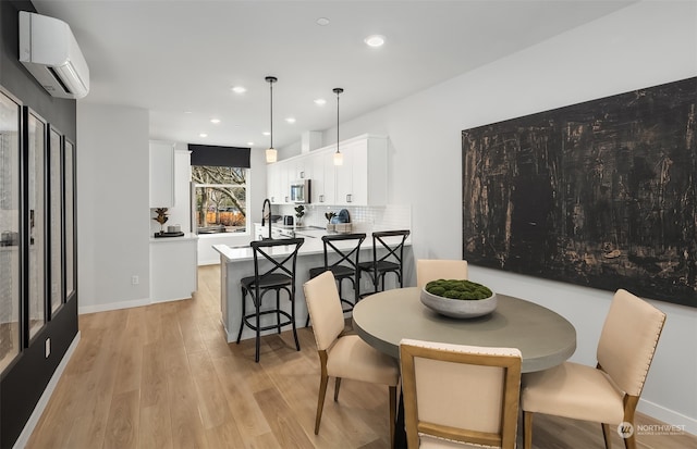 dining space featuring a wall unit AC, sink, and light hardwood / wood-style floors