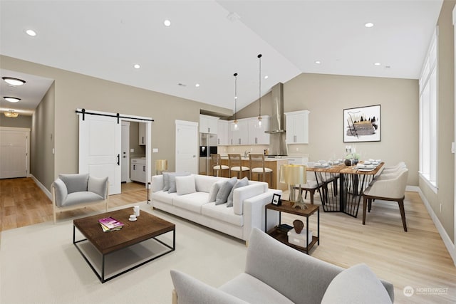 living room with a barn door, high vaulted ceiling, and light wood-type flooring