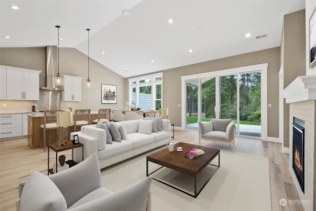 living room with high vaulted ceiling, a fireplace, and light hardwood / wood-style flooring