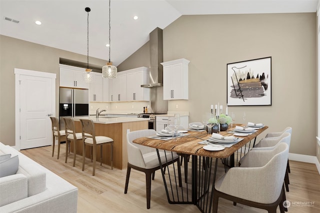 dining room with high vaulted ceiling, sink, and light hardwood / wood-style floors