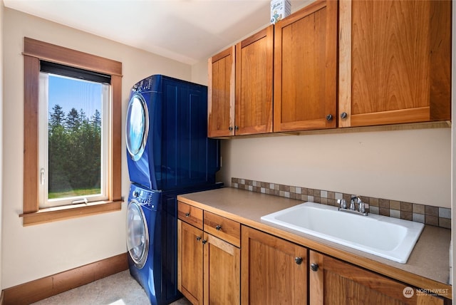 laundry area with sink, stacked washer / dryer, and cabinets