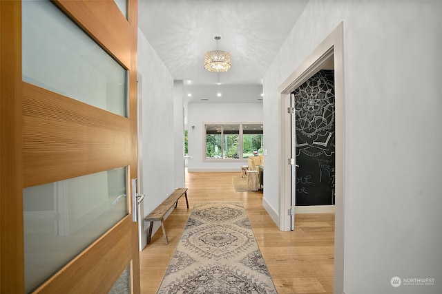 corridor with light wood-type flooring and an inviting chandelier