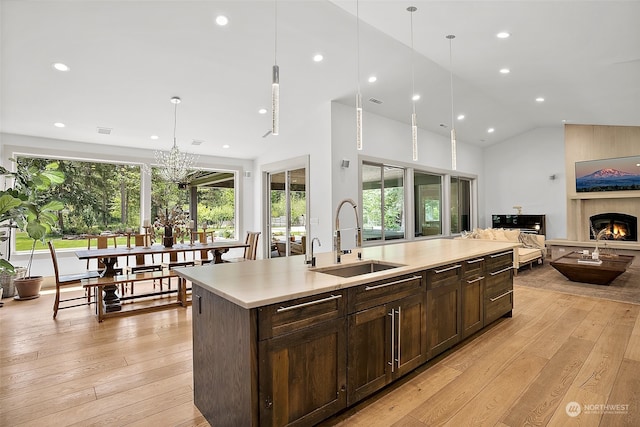 kitchen with light wood-type flooring, a center island with sink, a large fireplace, pendant lighting, and sink