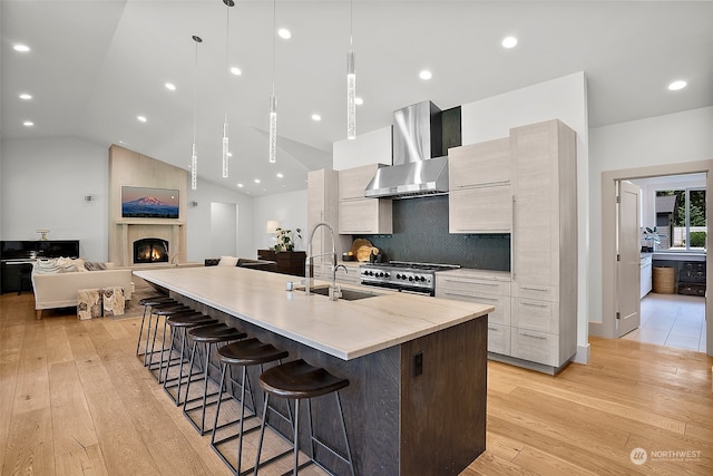 kitchen with vaulted ceiling, a fireplace, backsplash, wall chimney exhaust hood, and a kitchen island with sink