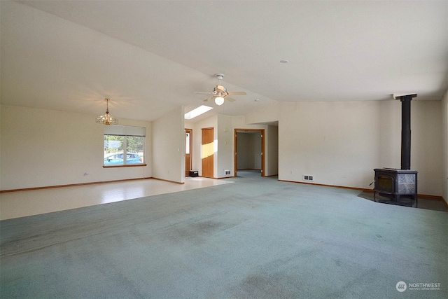 unfurnished living room featuring a wood stove, ceiling fan with notable chandelier, carpet, and vaulted ceiling