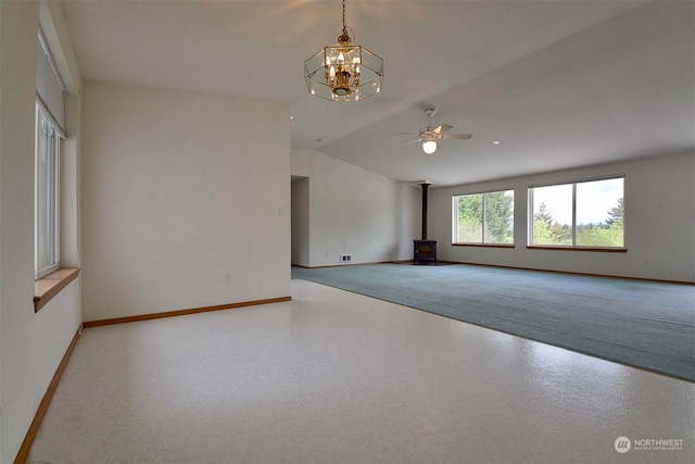 spare room with a wood stove, ceiling fan with notable chandelier, and vaulted ceiling