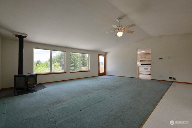 unfurnished living room featuring light carpet, vaulted ceiling, a wood stove, and ceiling fan