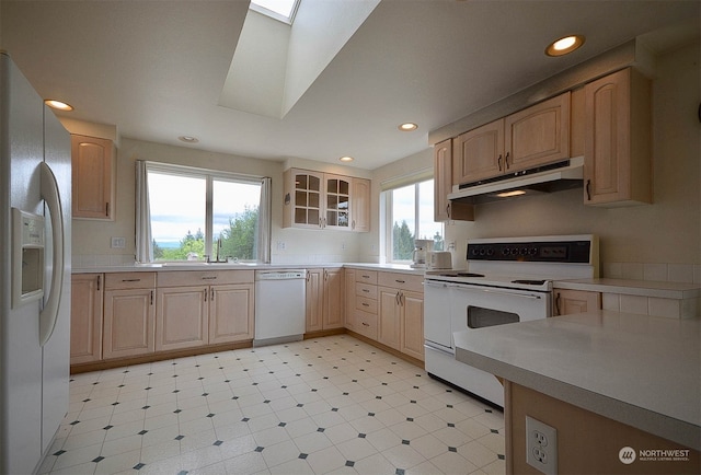 kitchen with a skylight, light brown cabinetry, and white appliances