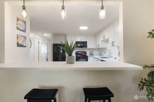 kitchen featuring decorative light fixtures, black appliances, sink, a breakfast bar, and white cabinetry