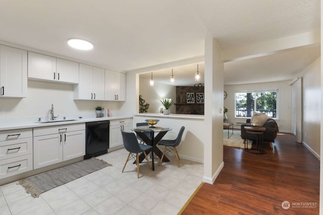 kitchen featuring light wood-type flooring, black dishwasher, hanging light fixtures, sink, and white cabinets