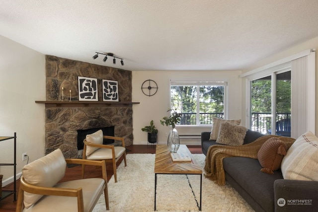 living room featuring a textured ceiling, a fireplace, baseboard heating, hardwood / wood-style flooring, and track lighting