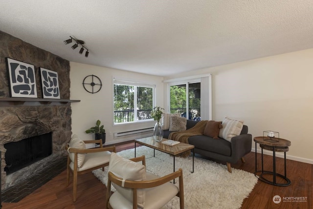 living room featuring a fireplace, a baseboard heating unit, rail lighting, dark wood-type flooring, and a textured ceiling