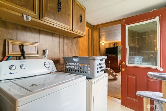 clothes washing area featuring light carpet, cabinets, wooden walls, and washer / clothes dryer