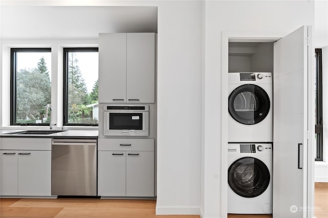 laundry area with sink, light hardwood / wood-style floors, and stacked washer and clothes dryer