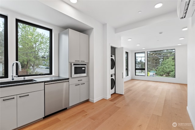 kitchen featuring light hardwood / wood-style flooring, appliances with stainless steel finishes, stacked washer and clothes dryer, an AC wall unit, and sink