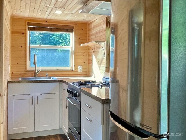 kitchen with white cabinetry, sink, wooden walls, and stainless steel appliances