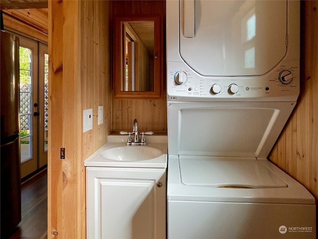 laundry room featuring sink, wooden walls, and stacked washer and dryer