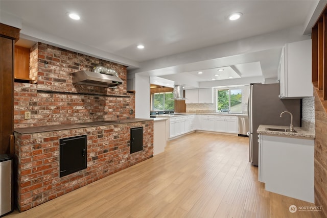 kitchen featuring wall chimney range hood, light hardwood / wood-style floors, backsplash, exhaust hood, and white cabinetry