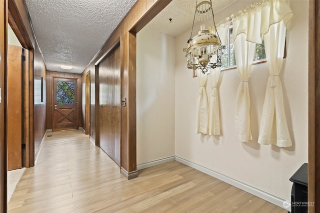 hall featuring light hardwood / wood-style floors, a textured ceiling, wooden walls, and a chandelier