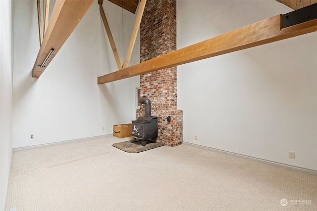 unfurnished living room with beamed ceiling, carpet flooring, a wood stove, brick wall, and high vaulted ceiling