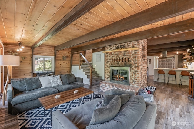 living room featuring beamed ceiling, wooden walls, a brick fireplace, and wood-type flooring