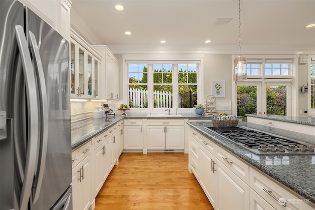 kitchen with appliances with stainless steel finishes, light hardwood / wood-style floors, backsplash, and dark stone countertops