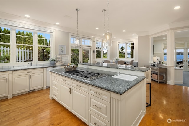 kitchen featuring light hardwood / wood-style floors, a kitchen island with sink, decorative light fixtures, stainless steel gas cooktop, and sink