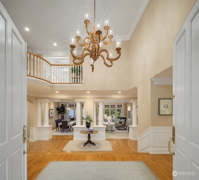 entrance foyer with a towering ceiling, a chandelier, hardwood / wood-style flooring, crown molding, and decorative columns