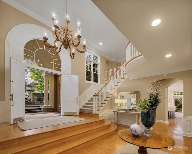 entrance foyer with crown molding, a towering ceiling, light wood-type flooring, and an inviting chandelier