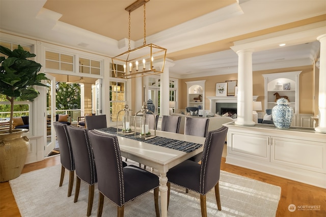 dining area with a tray ceiling, light hardwood / wood-style floors, an inviting chandelier, and ornate columns