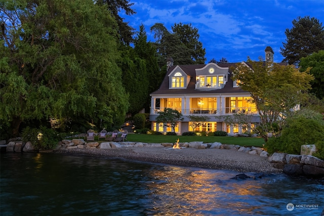 rear view of house with a balcony, a lawn, and a water view