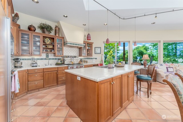 kitchen with tile counters, premium range hood, light tile floors, hanging light fixtures, and a center island