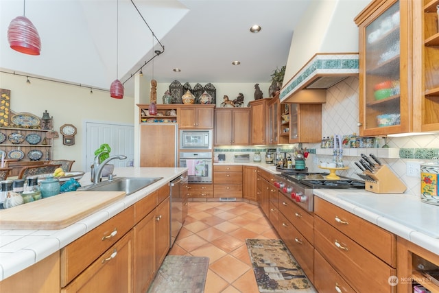 kitchen featuring stainless steel appliances, decorative light fixtures, premium range hood, sink, and tile countertops