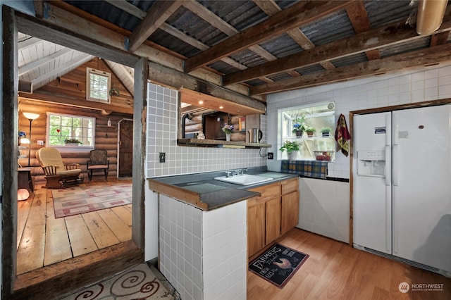 kitchen with light hardwood / wood-style floors, vaulted ceiling with beams, white refrigerator with ice dispenser, sink, and log walls